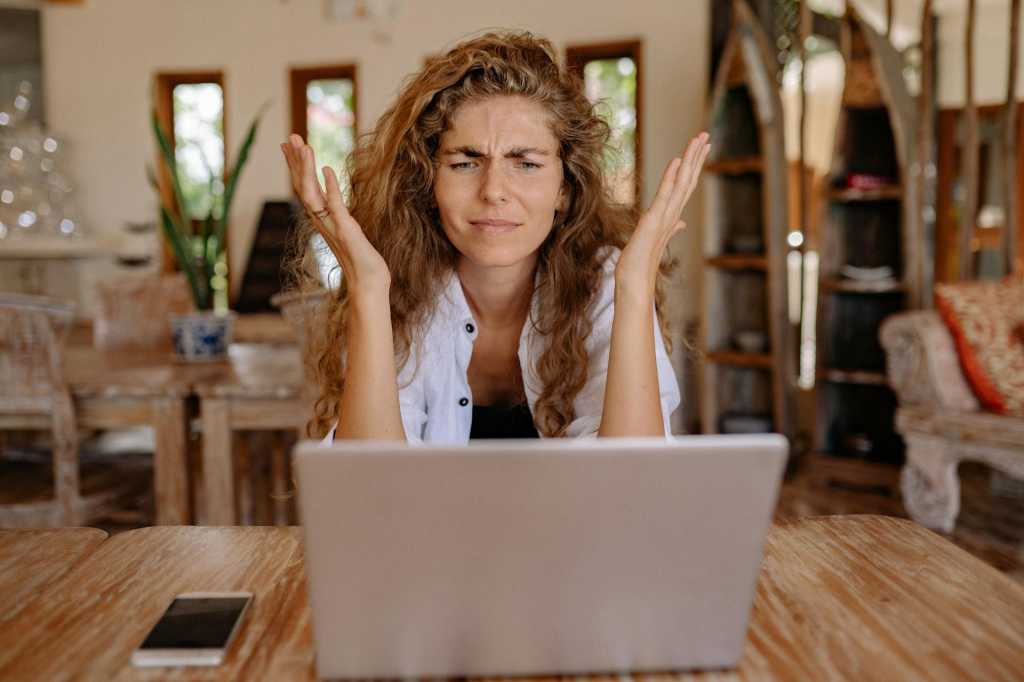 woman looking at laptop screen with hands thrown up in frustration