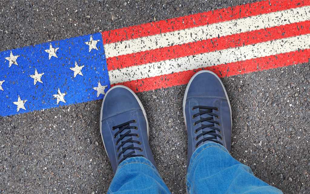legs and sneakers of someone standing next to an american flag painted on asphalt